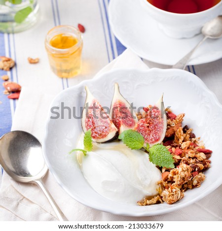 Honey glazed oat, goji berries granola with fresh figs and yogurt with a cup of tea on a textile blue and white background