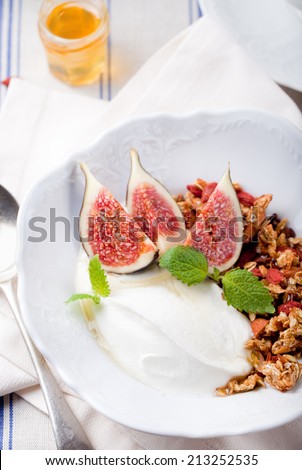 Honey glazed oat and goji berry granola with fresh figs and yogurt with a cup of tea on a textile blue and white background.
