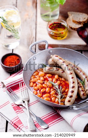 Grilled sausages with beans in tomato sauce in with rosemary and paprika in a vintage pan on a wooden background.