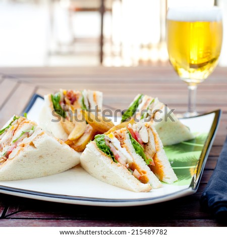 Club sandwich with french fries and  a glass of beer on a wooden table. Fast food.