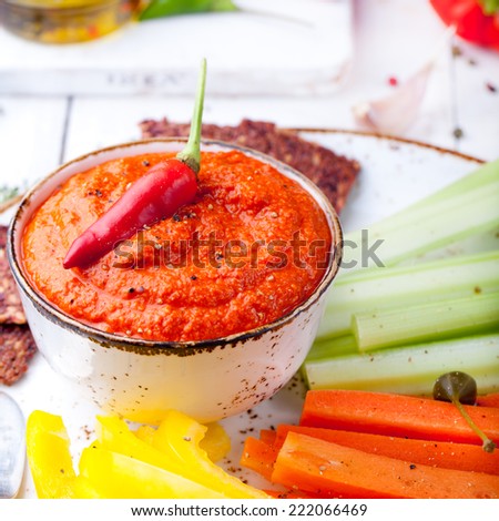 Roasted pepper dip, sauce, spread in a ceramic bowl with fresh carrot, celery sticks on a white wooden background