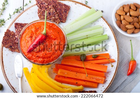 Roasted pepper dip, sauce, spread in a ceramic bowl with fresh carrot, celery sticks on a white wooden background
