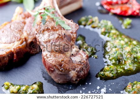 Grilled meat, mutton, lamb rack with fresh salad and sauce on black stone plate.
