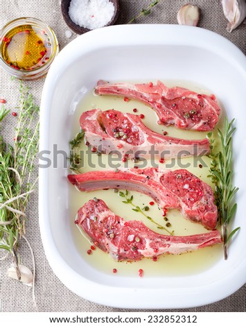 Raw meat, mutton, lamb rack with fresh herbs marinated in olive oil with herbs in a ceramic baking dish