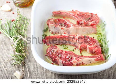 Raw meat, mutton, lamb rack with fresh herbs marinated in olive oil with herbs in a ceramic baking dish