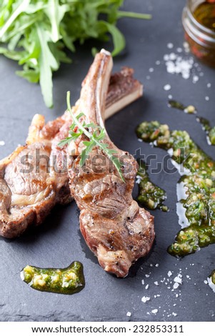Grilled meat, mutton, lamb rack with fresh salad and sauce on black stone plate.