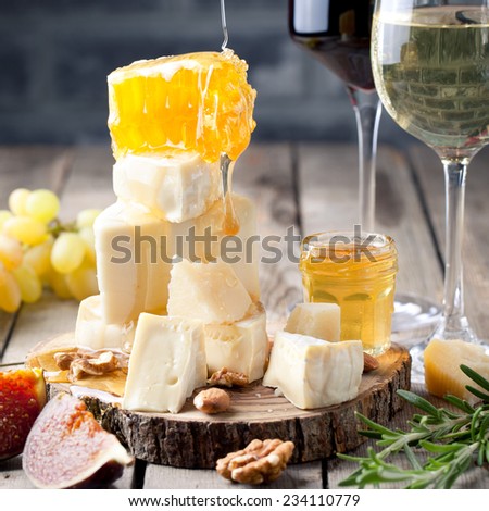 Grape, cheese, figs and honey with a glasses of red and white wine on a stone and wood background.