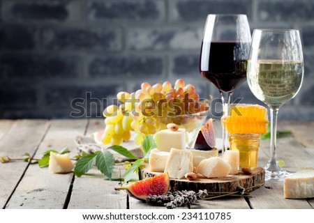 Grape, cheese, figs and honey with a glasses of red and white wine on a stone and wood background.