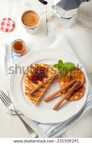 French toasts with orange marmalade, grilled apples and cinnamon sticks on a white plate with a cup of coffee. Traditional breakfast.