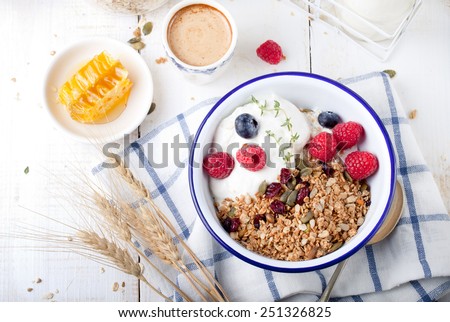 Healthy breakfast. Granola, muesli with pumpkin seeds, honey, yogurt and fresh berries in a ceramic bowl  with a cup of coffee on white background.