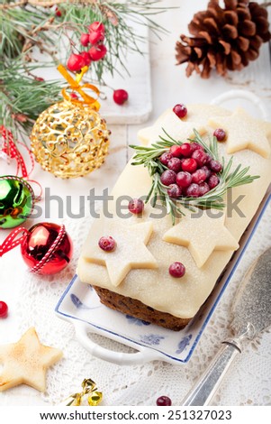 Traditional Christmas Fruit Cake pudding with marzipan and cranberry and rosemary decor on a Christmas decoration background
