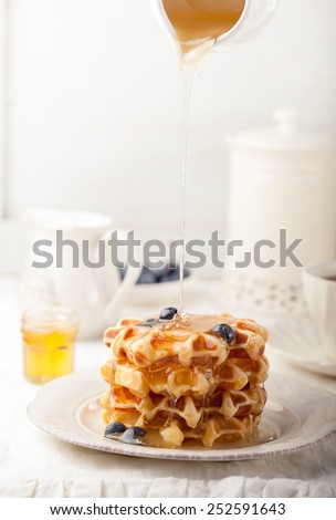 Honey pouring on a fresh waffles with blueberries Breakfast table.