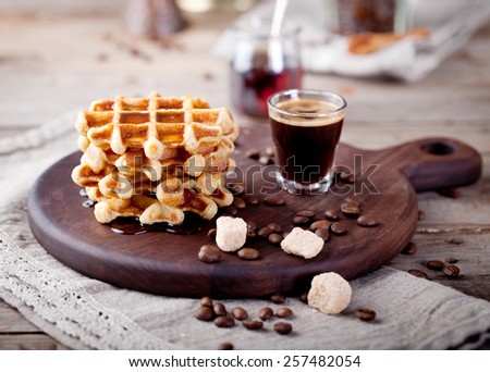 Fresh waffles with maple syrup and coffee on a wooden background.