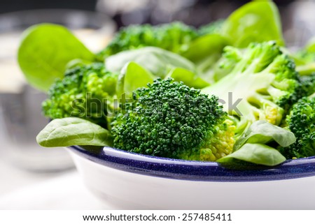 Broccoli, baby spinach and green beans salad in ceramic bowl with olive oil on a white wooden background.