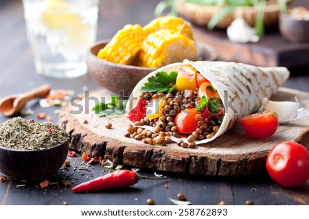 Vegan tortilla wrap, roll with grilled vegetables and lentil  and boiled corn cob on a wooden background