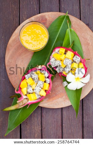 Tropical fruit salad in pitahaya, dragon fruit bowls with a glass of mango juice and flower on a wooden background