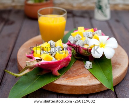 Tropical fruit salad in pitahaya, dragon fruit bowls with a glass of mango juice and flower on a wooden background