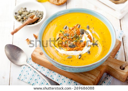 Roasted pumpkin and carrot soup with cream and pumpkin seeds on white wooden background. Copy space