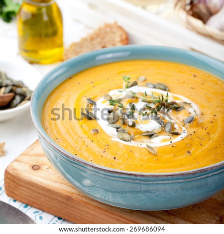 Roasted pumpkin and carrot soup with cream and pumpkin seeds on white wooden background. Copy space