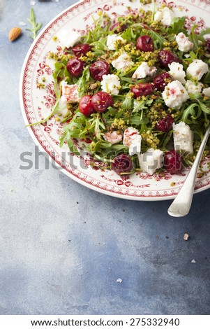 Salad with arugula, cherries and goat cheese on a blue background