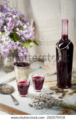 Blackcurrant homemade liquor on a wooden background with lilac flowers