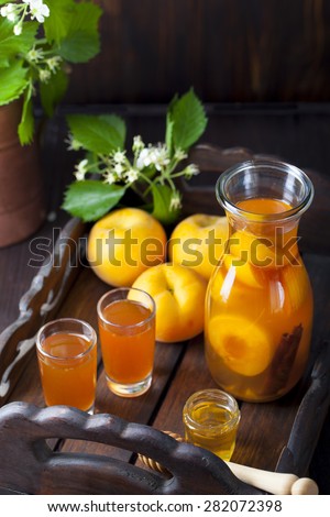 Apricot and cinnamon homemade liquor on a dark wooden background with fresh flowers