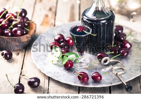 Cherry homemade liquor in a vintage bottle on a wooden background with fresh cherries.