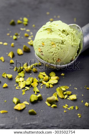 Pistachio ice cream scoop with pistachio nuts on a black stone background.
