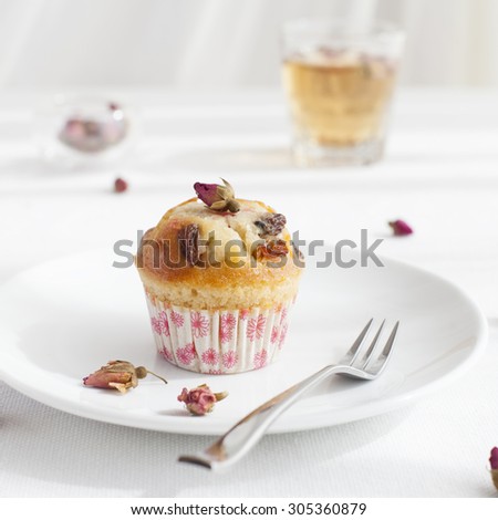 Muffin, mini cake, cup cake  on a white plate with a rose buds tea on a white textile background