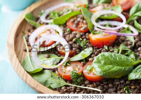 Lentil salad with cherry tomatoes, red onion and baby spinach in a wooden plate on a turquoise background