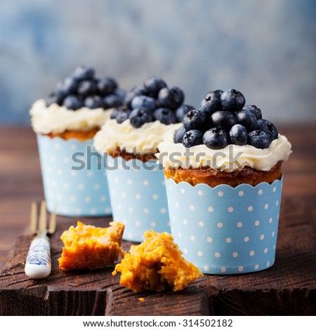 Carrot cupcakes  decorated with cream cheese frosting and fresh blueberries on a wooden background