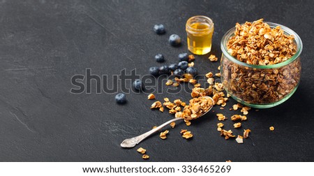 Healthy breakfast. Fresh granola, muesli with berries, honey in a glass jar on a black slate background. copy space