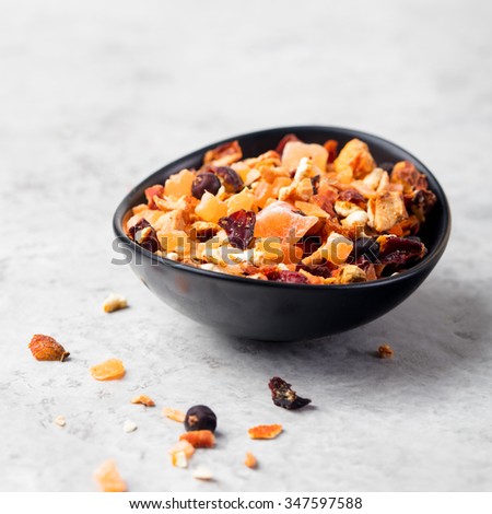 Dry fruit and spices tea: orange, lemon, apricot, apple, rose, juniper berry in a black bowl on a grey stone background