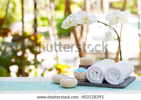 Spa and wellness massage setting Still life with candle, towel and stones Outdoor summer background with fresh white orchid Copy space