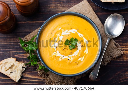 Pumpkin and carrot soup with cream and parsley on dark wooden background Top view