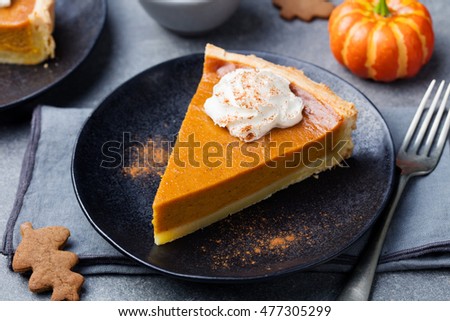 Pumpkin pie, tart made for Thanksgiving day with whipped cream on a black plate. Grey stone background