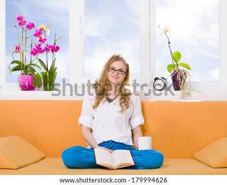 Relaxing with a book / Reader looking and smiling  at the camera holding her book and a cup