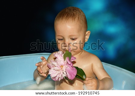 Little boy in bath with flower in hand on blue background.