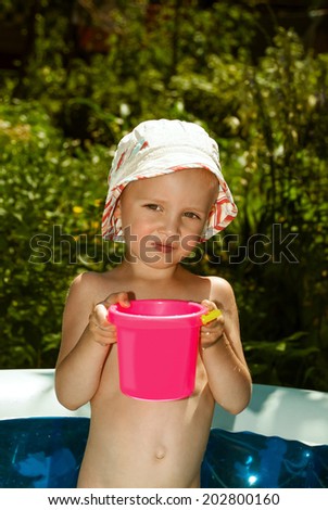 Small child in Panama in an inflatable pool with pink bucket of water.