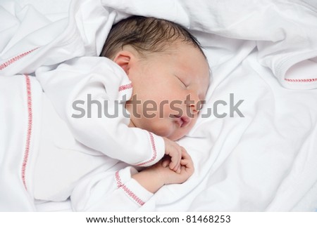 A young newborn baby is sleeping on a white bed with a blanket.