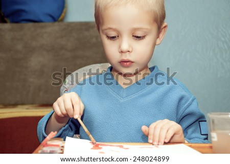Cute little child painting with colorful paints in home.