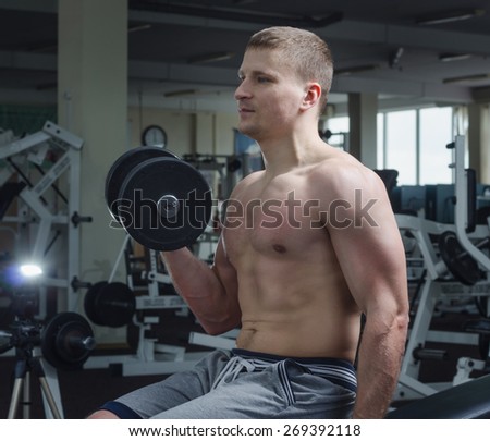 A young man in the gym performing an exercise one-arm dumbbell curl.