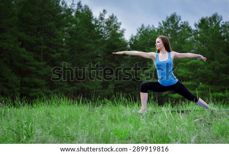 Young girl practicing yoga in nature in the woods on a background of green trees and grass.