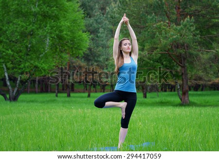 Young girl practicing yoga in nature in the woods on a background of green trees and grass. She balances on one leg.