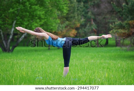 Young girl practicing yoga in nature in the woods on a background of green trees and grass. She balances on one leg.