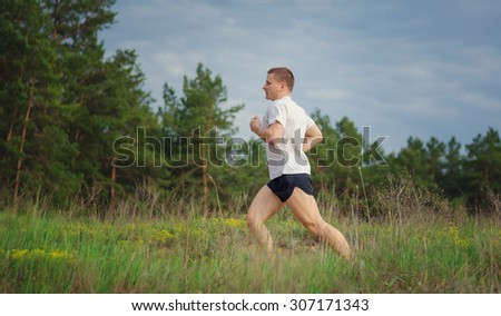 Young muscular man jogging outdoors, in the woods.