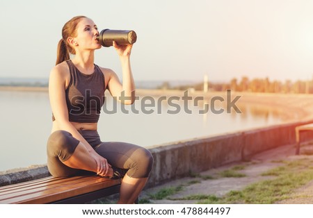 Young girl running after sitting on the bench. Sportswoman drinks from the shaker.