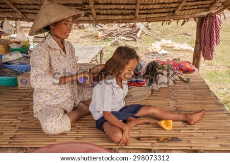 Mother combing daughter on a lounger under a canopy - December 02.2009 year: the family pottery village on vacation. Mum helps the little girl combing her hair in a pigtail and collect, Cambodia.