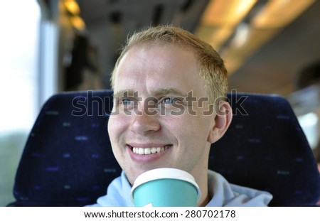 A young guy traveling by the train with cup of coffee - original