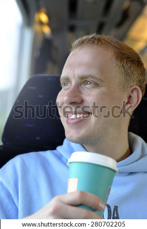 A young guy traveling by the train with cup of coffee - original